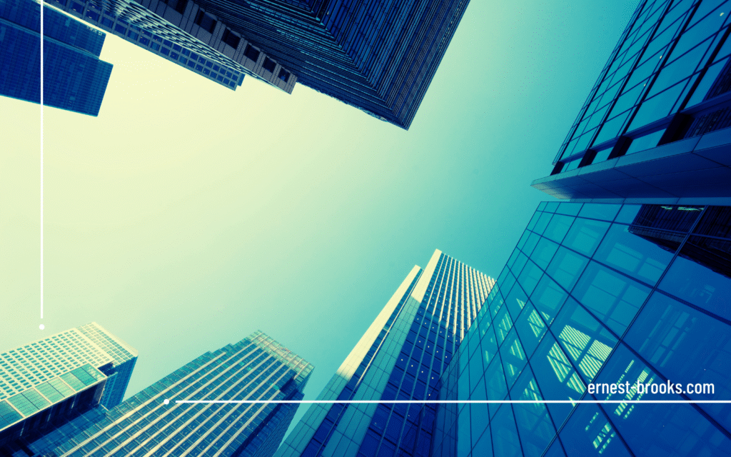 Modern glass and steel office buildings photographed from street level against clear blue sky, representing Ernest-Brooks London headquarters.